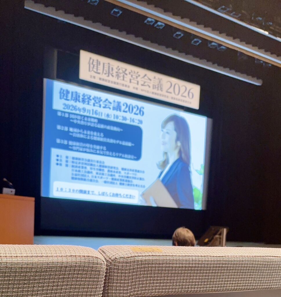 健康経営会議2026の案内が映し出された日経ホールの会場